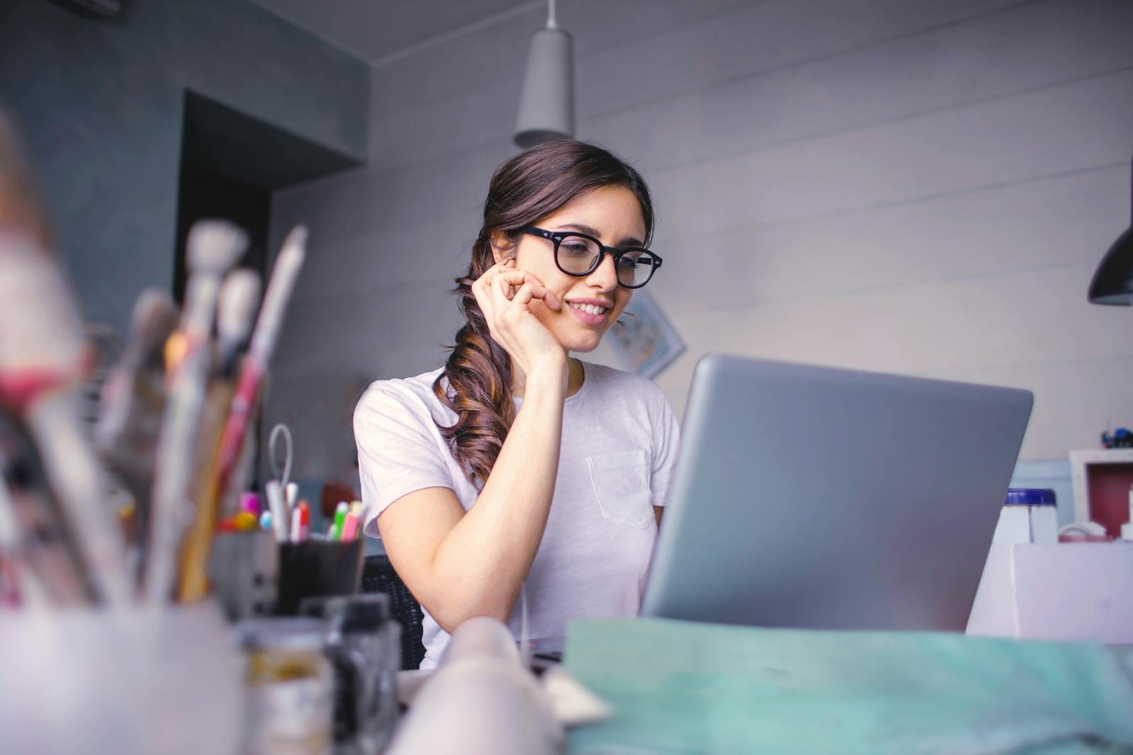 A cheerful woman in glasses works remotely on her laptop in a cozy home office setting. Cursos Online para você estar qualificado quanto aos requisitos exigidos pelas empresas! Ofertas que cabem no seu bolso!