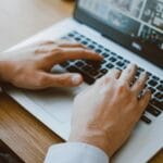 23 Vagas remotas na TecPar Close-up of a man's hands typing on a laptop keyboard, ideal for illustrating remote work or digital communication.