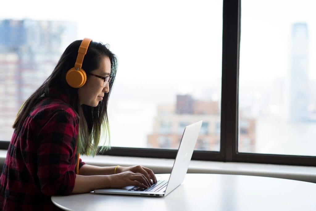 Operador de Telemarketing Home Office e mais Asian woman with headphones using laptop for remote work in a city setting.