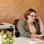 Vagas Remotas para Atendimento ao Cliente Professional woman in wheelchair working remotely on laptop and phone in a modern office.