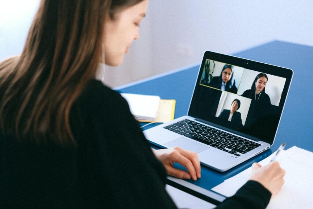 Home Office para Atendente e mais Empregos A woman engaging in a video conference using a laptop at home, taking notes.
