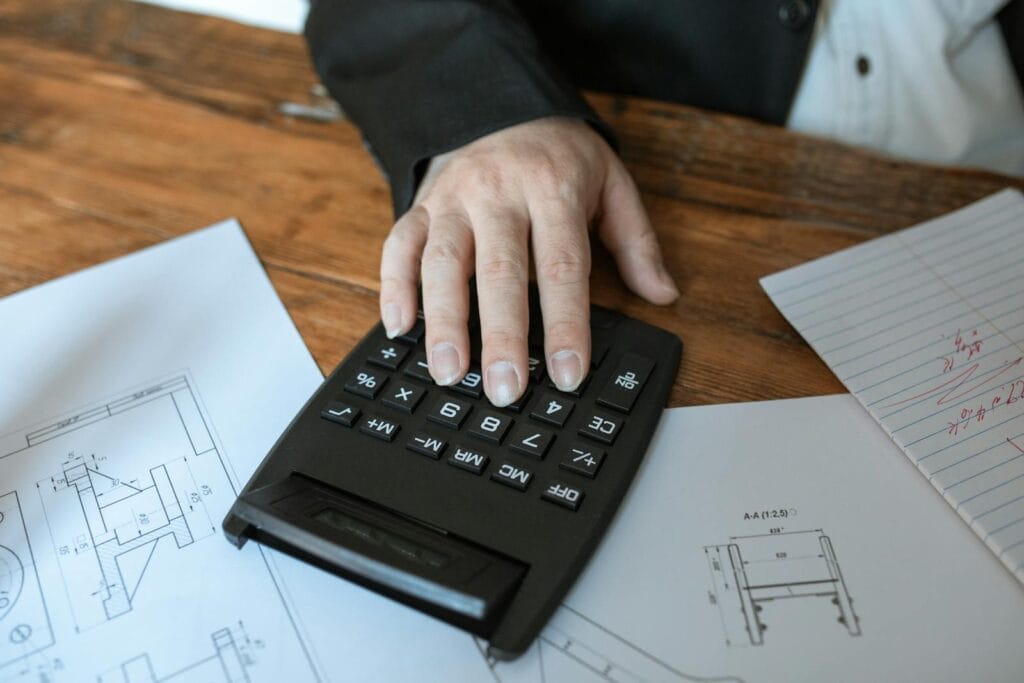 Vagas Remotas na JS Contadores Hand using calculator for architectural calculations on blueprints.