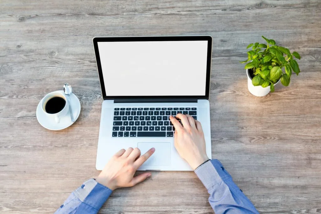 Vagas Remotas na Contmatic A comforting workspace with a laptop, coffee cup, and potted plant on a wooden desk.