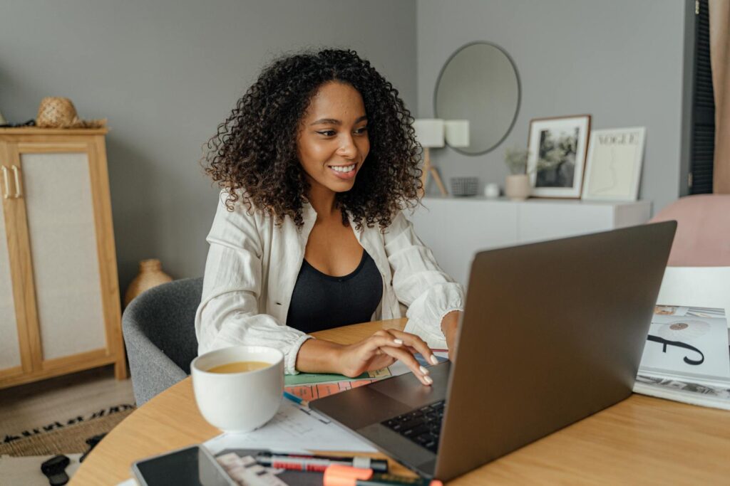Vagas Remotas na Capco A woman sits at a round table, working on a laptop with a coffee cup nearby in a cozy home office setting.