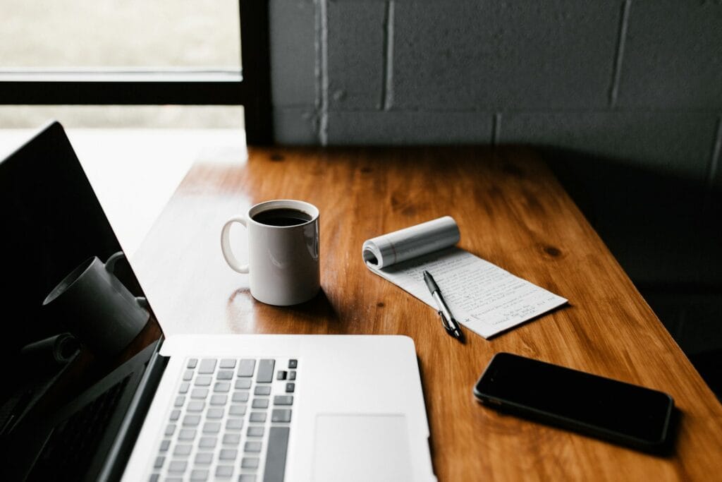 Assistente de Reservas e Executivo de Contas em Home Office MacBook Pro, white ceramic mug,and black smartphone on table