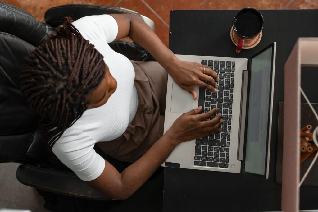 Home Office para Auxiliar Administrativo e mais oportunidades Overhead shot of a woman typing on a laptop at home, representing remote work.