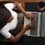 Home Office para Auxiliar Administrativo e mais oportunidades Overhead shot of a woman typing on a laptop at home, representing remote work.
