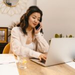 Vagas Remotas na Nomus Young woman multitasking with laptop and cellphone in home office setup.
