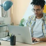 Vagas Remotas na Gran Cursos Man with dreadlocks working on laptop at desk.