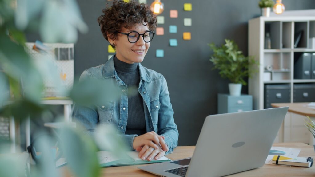 Vagas Remotas na Lynx A smiling woman with curly hair works at a laptop.