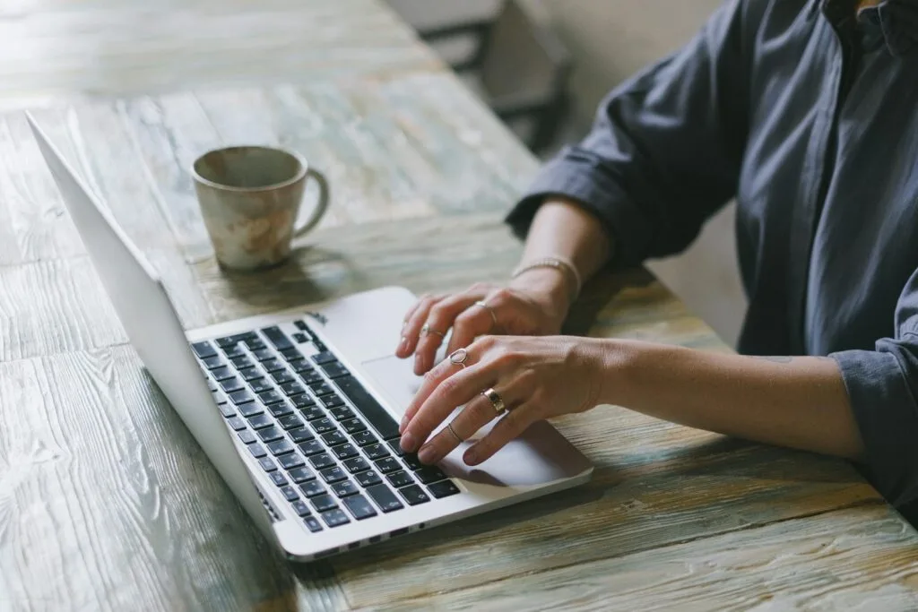 Auxiliar de Reservas Remoto e mais Vagas Efetivas em Home Office Crop faceless female freelancer in casual outfit sitting at table with cup of drink and surfing on laptop in light workspace