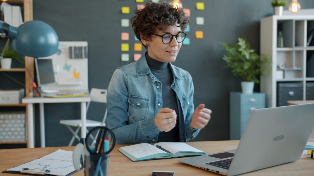 Vagas Remotas para Atendimento Woman gesturing while on a video call at desk.