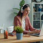 Vagas Remotas para Auxiliar Administrativo e mais! Young woman wearing headphones works on laptop at desk.