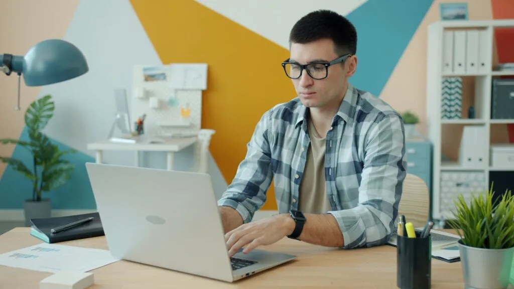 Vagas Remotas na Coruja Labs, com VA/VR de R$ 845,00 Man wearing glasses typing on a laptop at a desk.