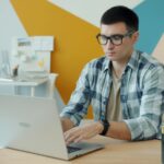 Vagas Remotas na Coruja Labs, com VA/VR de R$ 845,00 Man wearing glasses typing on a laptop at a desk.