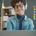 Analista de Suporte Técnico JR e mais Vagas Remotas Abertas! Woman wearing headphones smiles while looking at laptop.