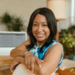 Vagas Remotas na ZG Soluções A smiling businesswoman sits confidently at her desk in a modern office setting.