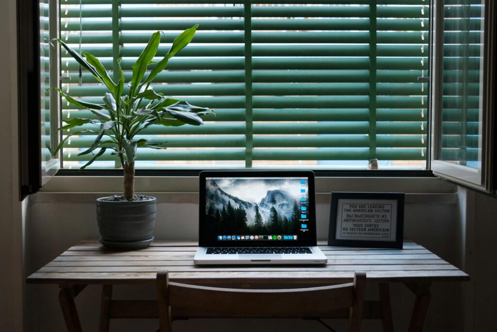 Home Office com R$ 950 de VA/VR Elegant home office desk setup with a laptop and a plant near a window. Ideal for remote work.