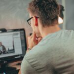 Home Office na Atlas com R$ 900,00 de VA/VR A man with glasses focused on editing a photo on his desktop computer in an office.