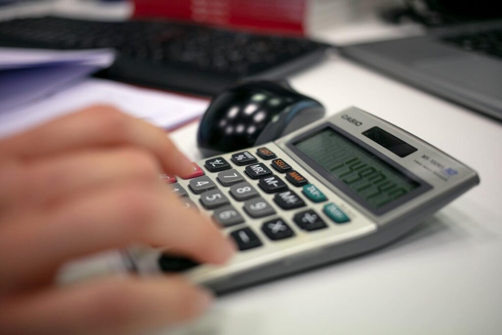 Assistente Fiscal e + vagas (CLT), com R$700,00 no Cartão Caju Close-up of a hand using a calculator on an office desk for accurate calculations.