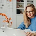 Home Office na Teleperformance, incluindo Aprendiz A woman in a bright sweater smiles while working on her laptop at home.