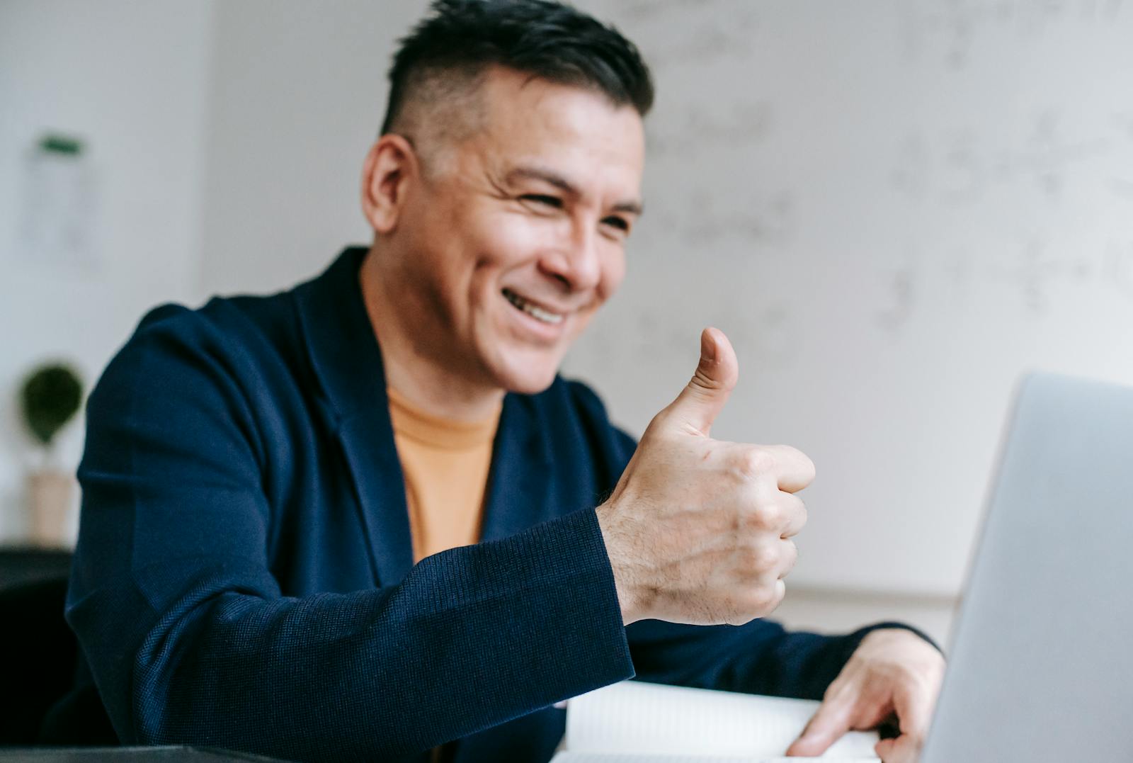 Trabalho Remoto com salário até R$ 6.200 (CLT) Smiling man giving thumbs up while working on laptop from home office, illustrating positive remote work experience.