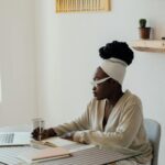 Vagas Remotas na Asaas, VA/VR de R$ 750,00 African American woman writing in a journal while working from home with a laptop.