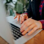 Home Office para Analista de Atendimento Júnior e mais! Hands typing on a laptop keyboard, close-up view, in a casual indoor setting.