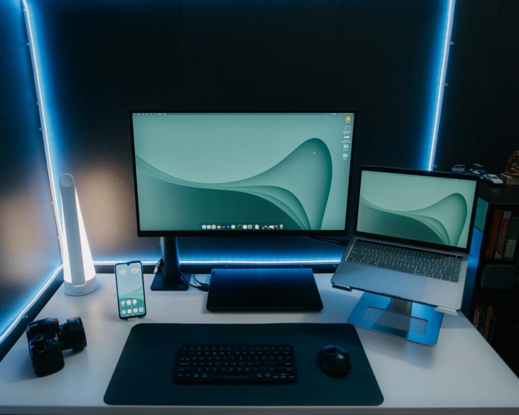 Vagas Remotas na Yampi com R$ 1047 de VR A sleek and modern desk setup featuring a monitor, laptop, and ambient lighting, perfect for productivity.
