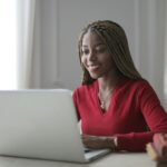 Vagas Remotas na VExpenses, VA/VR de R$ 1.200 Young black woman happily working on a laptop indoors, showcasing a modern remote work setup.