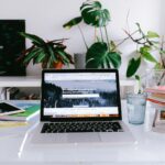 Vagas Remotas na Netbr com R$ 890,00 de VA/VR A clean and bright home office desk with a laptop, books, and plants, perfect for freelancers or remote work.