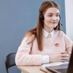 Sucesso do Cliente JR e + remotas com VA de R$ 718,00 + comissões! Smiling woman in pink sweater working remotely as a customer service agent.