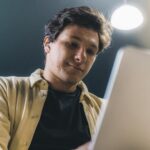 Young man working on a laptop indoors, smiling and focused, representing a modern freelance lifestyle.