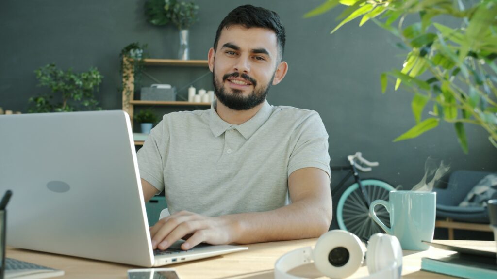 Home Office com até 2,5 salário em bônus semestral A man smiles while working on a laptop.