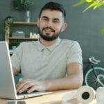 Home Office com até 2,5 salário em bônus semestral A man smiles while working on a laptop.