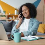 Home Office na Sami Saúde, com VA/VR de R$ 800,00 Woman talking on phone while working on laptop at desk.