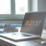 Remotas com salário até R$ 16.000 (CLT) A serene workspace featuring a laptop with digital time display, perfect for productivity and focus.