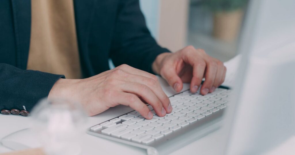 Home Office na Segware Close-up of hands typing on a white keyboard in an office setting. Ideal for business or technology themes.