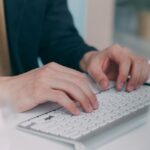 Home Office na Segware Close-up of hands typing on a white keyboard in an office setting. Ideal for business or technology themes.