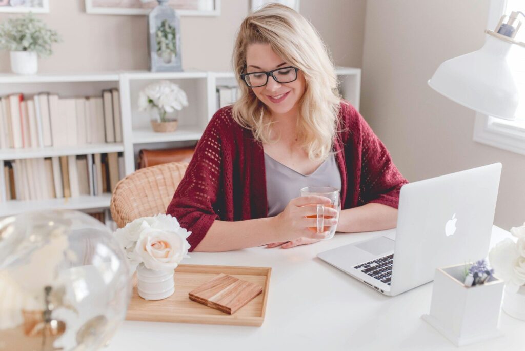 Vagas Remotas na Monks woman smiling holding glass mug sitting beside table with MacBook