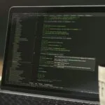 Vagas Remotas na FourHands, com salário até R$ 13.500 Laptop screen displaying lines of code with a coffee mug.