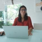Vagas Remotas na Minsait Woman works on laptop at a bright, modern table.