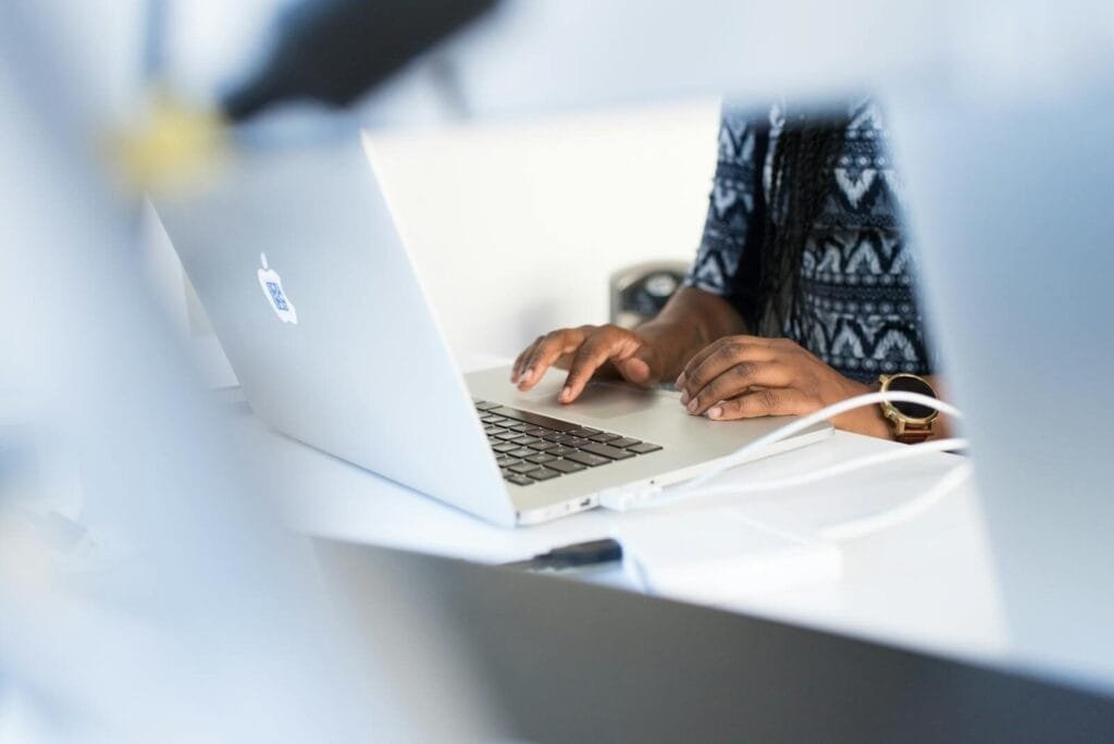 Remotas na Atento Escalada, salário até R$ 5.000,00 Woman typing on a laptop at a desk in a modern office setting, focused on work.