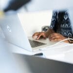 Remotas na Atento Escalada, salário até R$ 5.000,00 Woman typing on a laptop at a desk in a modern office setting, focused on work.