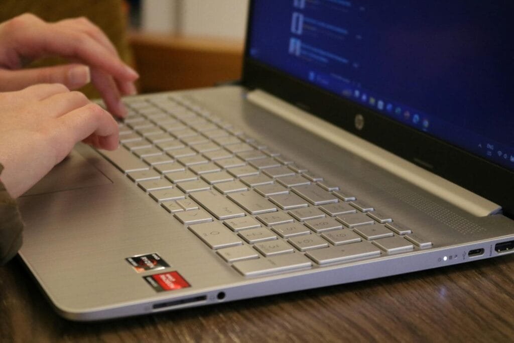 Remotas com salário até R$ 10.000 Hands typing on a silver laptop keyboard, showcasing productivity and technology.