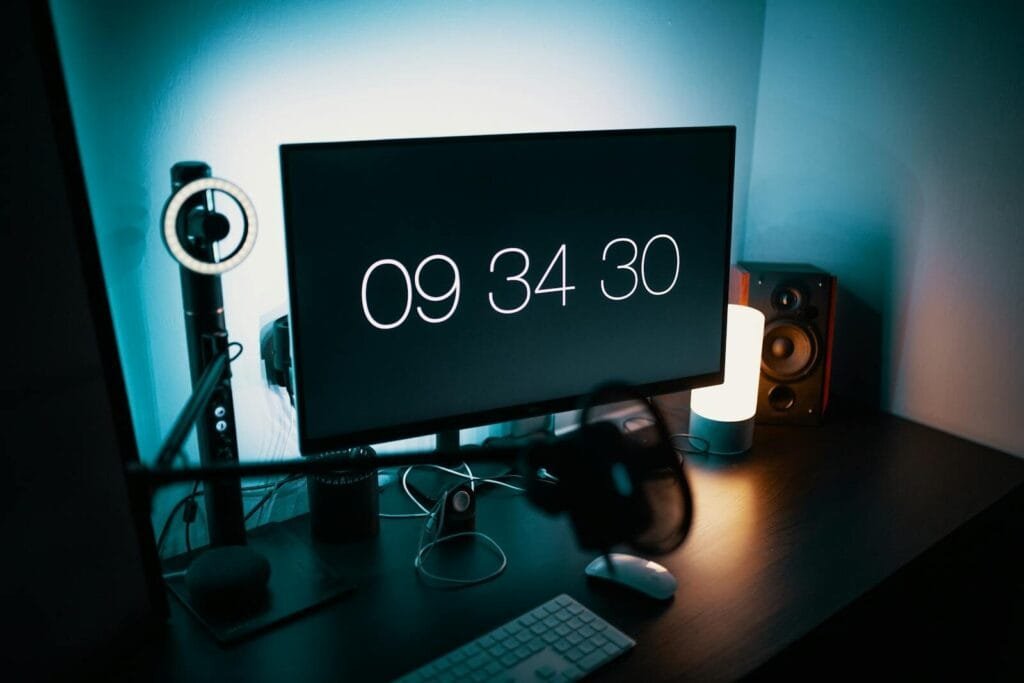 Remotas com salário até R$ 12.000 (CLT) A sleek desk setup featuring a large monitor with a digital clock and ambient lighting.