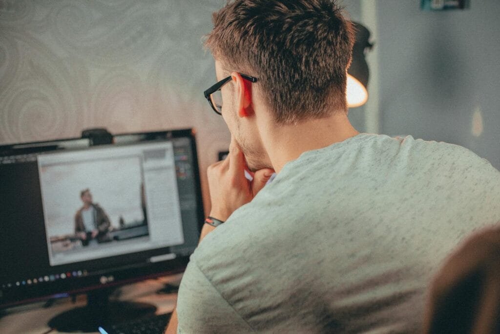 Assistente de Suporte e +, com VA/VR de R$ 1.000 A man with glasses focused on editing a photo on his desktop computer in an office.
