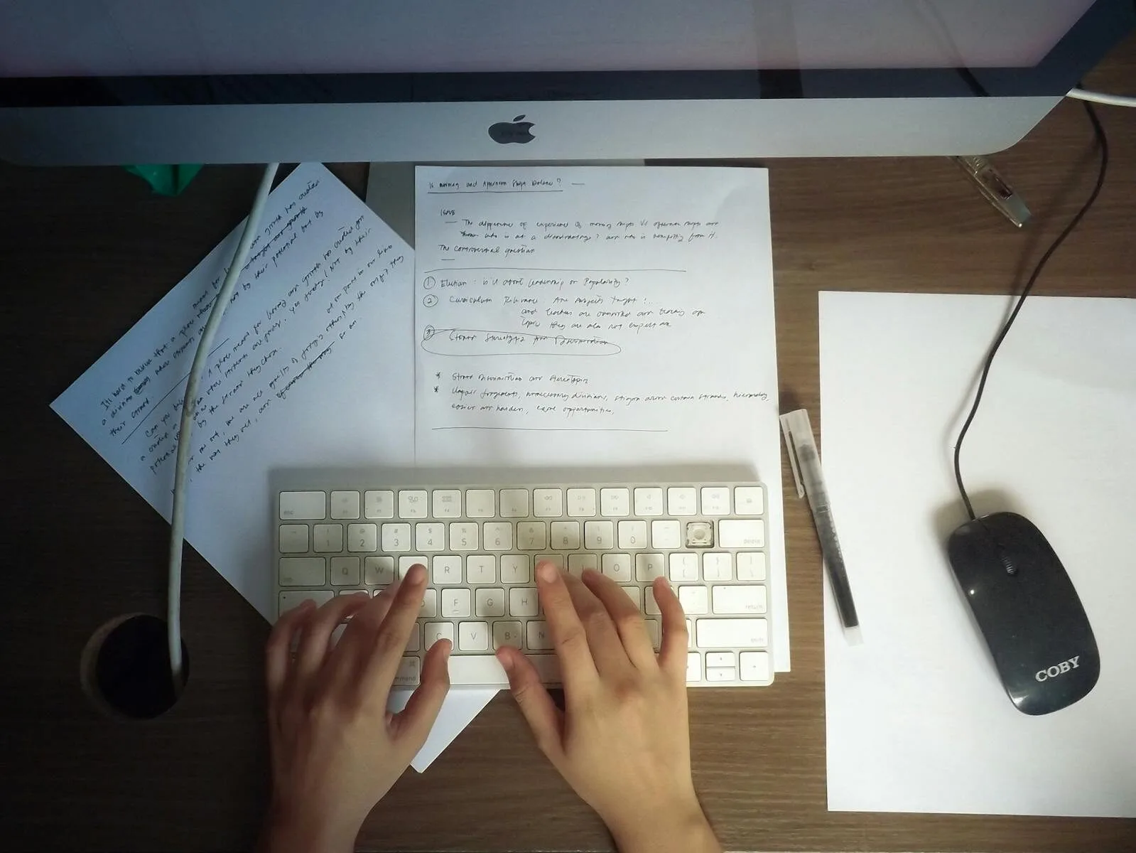 Home Office com salário até R$ 6.000 (CLT) Hands typing on a keyboard at a wooden desk with papers and computer mouse visible.