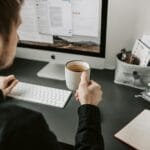 Remotas no Grupo Casas Bahia A man enjoying coffee while working on a computer indoors. Ideal for work-from-home scenarios.