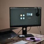 Vagas Remotas para Atendimento e +, com R$ 900,00 de VA/VR Contemporary computer with headphones hanging on monitor placed on table with laptop keyboard and mouse at convenient workplace in room